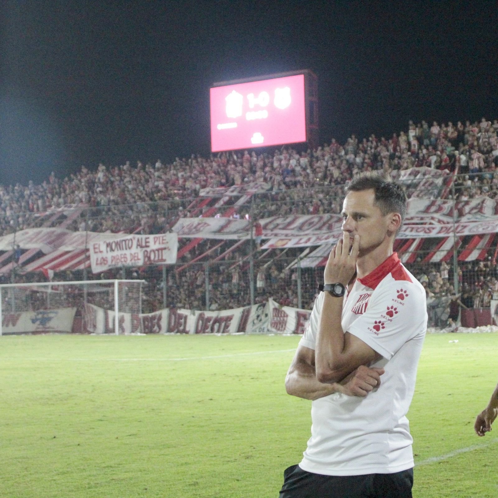 Juan Manuel Cavallo al borde del campo en un partido nocturno de San Martín de Tucumán, con la tribuna llena de fondo